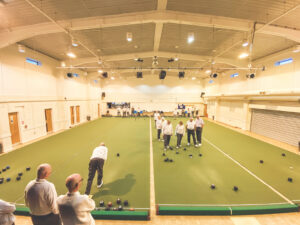 Wide view of the indoor bowls facility with players gathered on the green