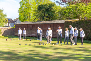 Club members in white bowling shirts lined up along the outdoor green at Swanscombe Park, with the clubhouse visible