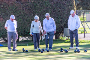 Wide view of the outdoor bowling green at Swanscombe Park with members playing and the clubhouse in the background