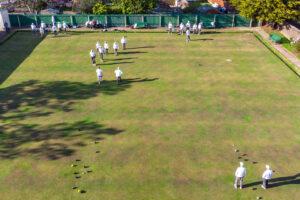 Aerial view of the outdoor green with multiple active games taking place simultaneously, spectators visible around the perimeter