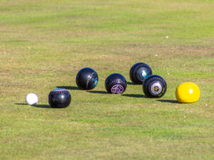 Close-up of black bowls arranged around the white jack on the outdoor grass green — a typical end in lawn bowls